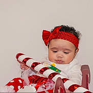 Adanna joined the competition — help win amazing prizes! baby, bow, candy_cane, chair, child, curly_hair, cute, festive, holding, holiday, indoors, infant, looking_down, portrait, props, red_headband, red_skirt, seated, tulle, white_shirt