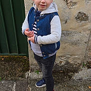 Nolan participe au concours pour gagner de l'argent avec cette photo : boy, casual_clothing, child, curious_expression, daylight, denim_jacket, fashion, ground, hoodie, jeans, outdoor, pavement, person, side_view, sneakers, standing, stone_wall, striped_shirt, urban, young