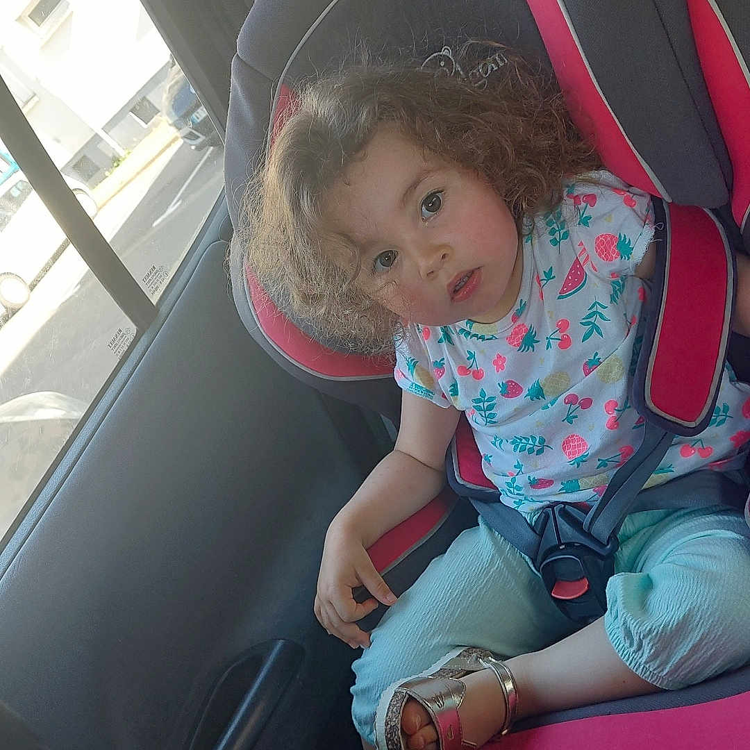 élyanor a rejoint le concours — aidez-le/la à gagner de superbes lots ! blue_pants, car_interior, car_seat, casual_clothing, child, curly_hair, daylight, gray, parking_lot, person, pink, road, safety, sandal, seat, seatbelt, toddler, vehicle, window, young_child