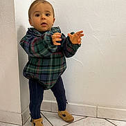 Julen a rejoint le concours — aidez-le/la à gagner de superbes lots ! toddler, child, standing, plaid_jacket, navy_leggings, brown_shoes, indoor, tile_floor, white_wall, curious, young_child, person, small_child, portrait, casual_clothing, cute, baby, exploring, corner, home