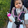 Lilyana joined the competition — help win amazing prizes! toddler, child, milk_bottle, stroller, outdoor, grass, fleece_clothing, checkered_pattern, pink, face, curly_hair, seat_belt, baby, person, nature, park, expressionless, hand, cute, young