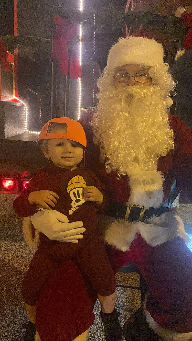 Kenneth joined the competition — help win amazing prizes! automotive_lighting, beard, christmas, costume, event, facial_hair, fictional_character, fun, fur, happy, hat, headgear, headwear, holiday, lap, moustache, person, santa_claus, standing, toddler