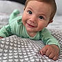baby, child, smiling, face, eyes, hand, blanket, heart_pattern, bed, indoors, cute, happy, green_clothing, infant, portrait, closeup, skin, head, young_child, lying_down