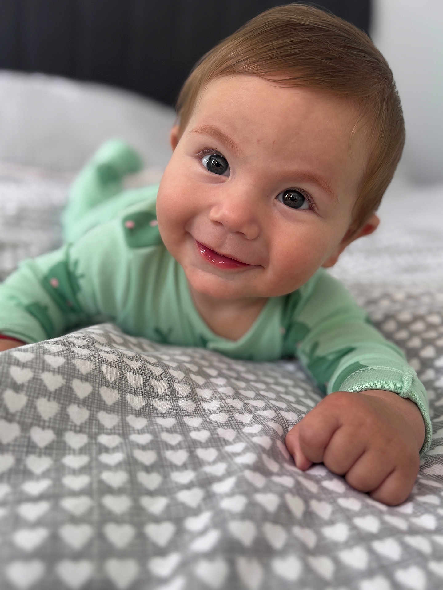Eric joined the competition — help win amazing prizes! baby, child, smiling, face, eyes, hand, blanket, heart_pattern, bed, indoors, cute, happy, green_clothing, infant, portrait, closeup, skin, head, young_child, lying_down