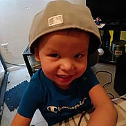 Mario is registered to the contest to win money with this photo: child, boy, smiling, cap, hat, tshirt, champion_brand, indoor, room, floor, carpet, shelf, toy_figurine, electronics, cable, face, portrait, happy, playful, home