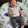 baby, infant, smiling, onesie, pants, socks, blanket, dinosaur_pattern, cute, happy, child, lying_down, soft_texture, indoor, cozy, person, face, head, small_hands, feet