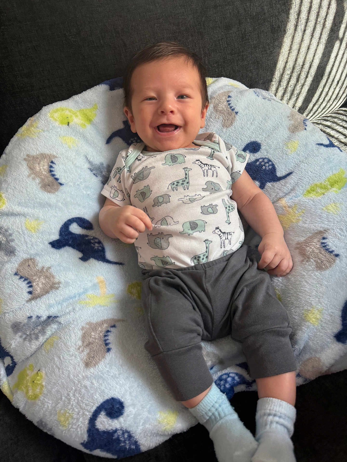 Axel joined the competition — help win amazing prizes! baby, infant, smiling, onesie, pants, socks, blanket, dinosaur_pattern, cute, happy, child, lying_down, soft_texture, indoor, cozy, person, face, head, small_hands, feet