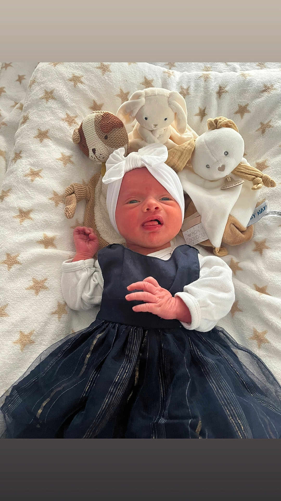 Alwena participe au concours pour gagner de l'argent avec cette photo : baby, infant, plush_toy, blanket, star_pattern, headband, dress, white_sleeves, lying_down, cute, soft_toys, expression, tongue_out, cozy, indoors, child, newborn, fabric, comfort, adorable