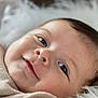 baby, infant, face, smile, close_up, soft, blanket, fluffy, cute, young_child, skin, eyes, head, portrait, lying_down, warm, comfort, expression, natural_light, cozy