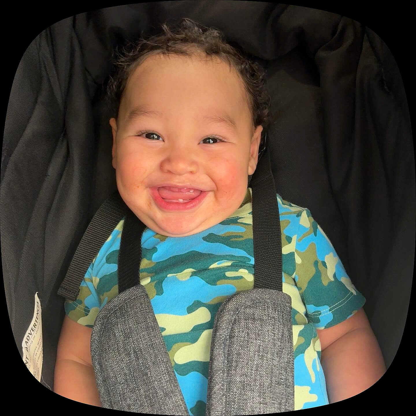Xylo-King is registered to the contest to win money with this photo: baby, child, smiling, curly_hair, car_seat, camouflage_shirt, happy, face, infant, safety_harness, cute, portrait, young_child, seat_strap, indoor, close_up, person, apparel, cheerful, toddler