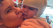 Kehlani is registered to the contest to win money with this photo: baby, child, woman, kiss, helmet, indoor, people, hug, affection, cute, love, protective_gear, pink_clothing, portrait, face, expression, ceiling, light, casual, holding
