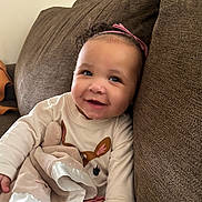Kehlani is registered to the contest to win money with this photo: baby, child, smile, couch, blanket, headband, pink, clothing, indoors, happy, face, person, soft_toy, comfort, young_child, seated, home, cute, portrait, cozy