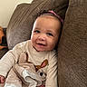 baby, child, smile, couch, blanket, headband, pink, clothing, indoors, happy, face, person, soft_toy, comfort, young_child, seated, home, cute, portrait, cozy