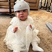 Kehlani joined the competition — help win amazing prizes! baby, child, helmet, white_dress, socks, carpet, living_room, couch, table, furniture, floor, person, indoors, cute, sitting, protective_gear, homedecor, household_items, headwear, soft_lighting