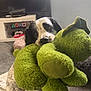 dog, plush_toy, green_toy, carpet, living_room, television, gaming_console, window, curtains, black_and_white_dog, pet, indoor, cute, playful, animal, fur, ears, floor, home, toy