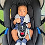 baby, car_seat, child, infant, safety_harness, pacifier_clip, blue_socks, curly_hair, outdoor, grass, sidewalk, black_car_seat, clothing, person, cute, seatbelt, straps, hands, feet, expression