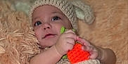 Orion is registered to the contest to win money with this photo: baby, child, knitted_hat, crocheted_toy, orange_carrot, soft_texture, fluffy_blanket, cute, smiling, portrait, indoor, close_up, hand, face, cozy, warm_colors, infant, happy, cuddly, resting