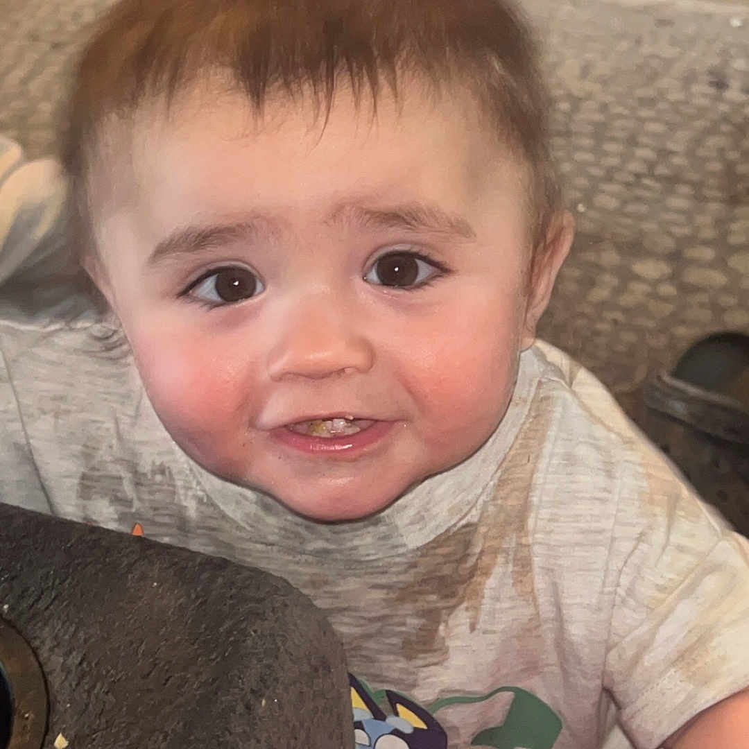 Westley is registered to the contest to win money with this photo: toddler, child, indoor, face, curious, messy, shirt, red_cushion, wood_floor, rug, person, baby, smiling, cute, young_child, expression, closeup, furniture, home, playful