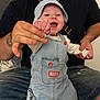 baby, adult, denim_overall, hat, marvel, spiderman, smile, happy, indoor, couch, tattoo, hand_holding, child, person, clothing, casual, jeans, facial_hair, beard, seated