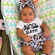 Kamryn is registered to the contest to win money with this photo: baby, child, infant, smiling, tongue_out, portrait, seated, bouncer, baby_chair, headband, bow, patterned_clothing, skirt, socks, cartoon_print, colorful, indoor, playful, cute, happy