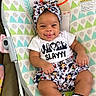baby, child, infant, smiling, tongue_out, portrait, seated, bouncer, baby_chair, headband, bow, patterned_clothing, skirt, socks, cartoon_print, colorful, indoor, playful, cute, happy