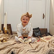 Cataleya participe au concours pour gagner de l'argent avec cette photo : baby, blanket, book, bow, candles, child, cozy, cute, decor, door, floor, golden_candle_holder, happy, headband, indoor, portrait, reading, sitting, smile, white_clothing