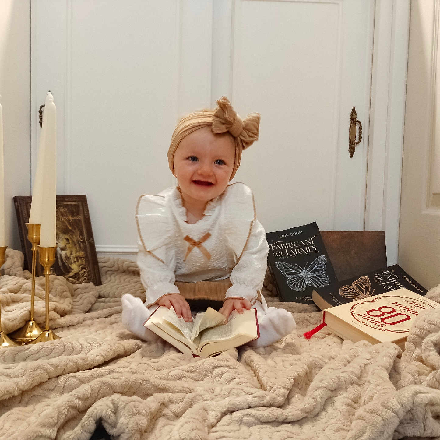 Cataleya participe au concours pour gagner de l'argent avec cette photo : baby, blanket, book, bow, candles, child, cozy, cute, decor, door, floor, golden_candle_holder, happy, headband, indoor, portrait, reading, sitting, smile, white_clothing