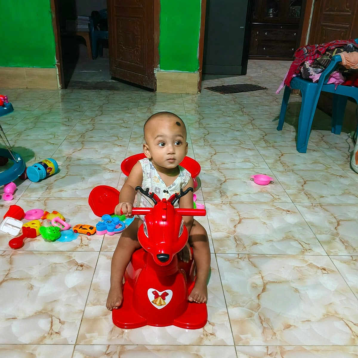 Mohammad Ridwan is registered to the contest to win money with this photo: baby, cabinet, child, colorful, curious, floor_tiles, flooring, footwear, furniture, green_wall, head, indoor, person, plastic_chair, playtime, rocking_horse, scattered_toys, toddler, toy, wooden_door