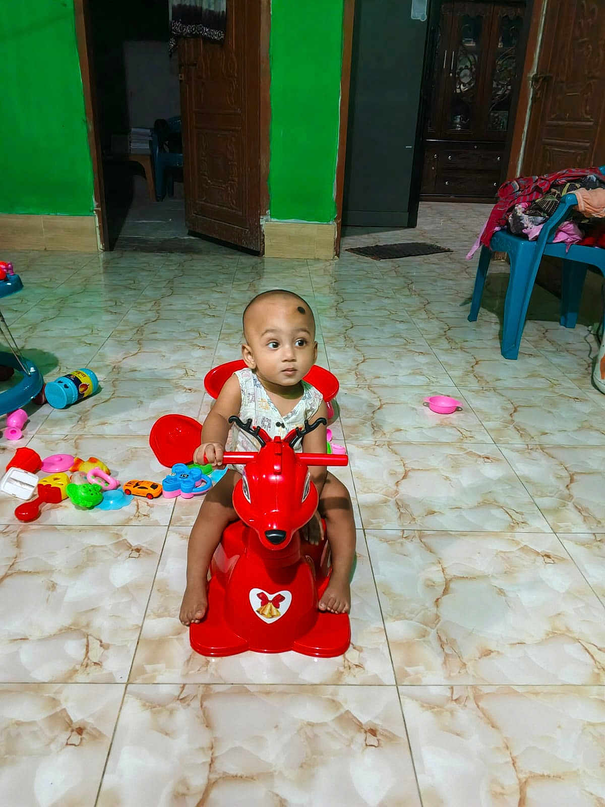 Mohammad Ridwan is registered to the contest to win money with this photo: toddler, child, toy, rocking_horse, indoor, floor_tiles, green_wall, wooden_door, plastic_chair, scattered_toys, curious, baby, playtime, furniture, footwear, cabinet, colorful, flooring, person, head