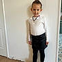 child, girl, standing, white_sweater, black_skirt, black_leggings, white_boots, smiling, indoor, wooden_floor, plain_wall, necklace, fashion, portrait, young, cute, hair_up, earrings, casual, confident