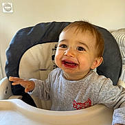 Maé participe au concours pour gagner de l'argent avec cette photo : baby, high_chair, smiling, indoor, child, person, clothing, face, happy, young_child, home, furniture, seat, cute, expression, infant, portrait, table, hand, light