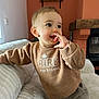 Maé a rejoint le concours — aidez-le/la à gagner de superbes lots ! toddler, child, indoor, couch, sweater, pants, face, hand, smiling, curious, furniture, home, window, light, cozy, portrait, baby, happy, person, casual_clothing