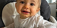Maé a rejoint le concours — aidez-le/la à gagner de superbes lots ! toddler, child, high_chair, smile, happy, face, hand, white_shirt, indoor, baby, person, cute, expression, young_child, skin, eyes, mouth, furniture, room, home
