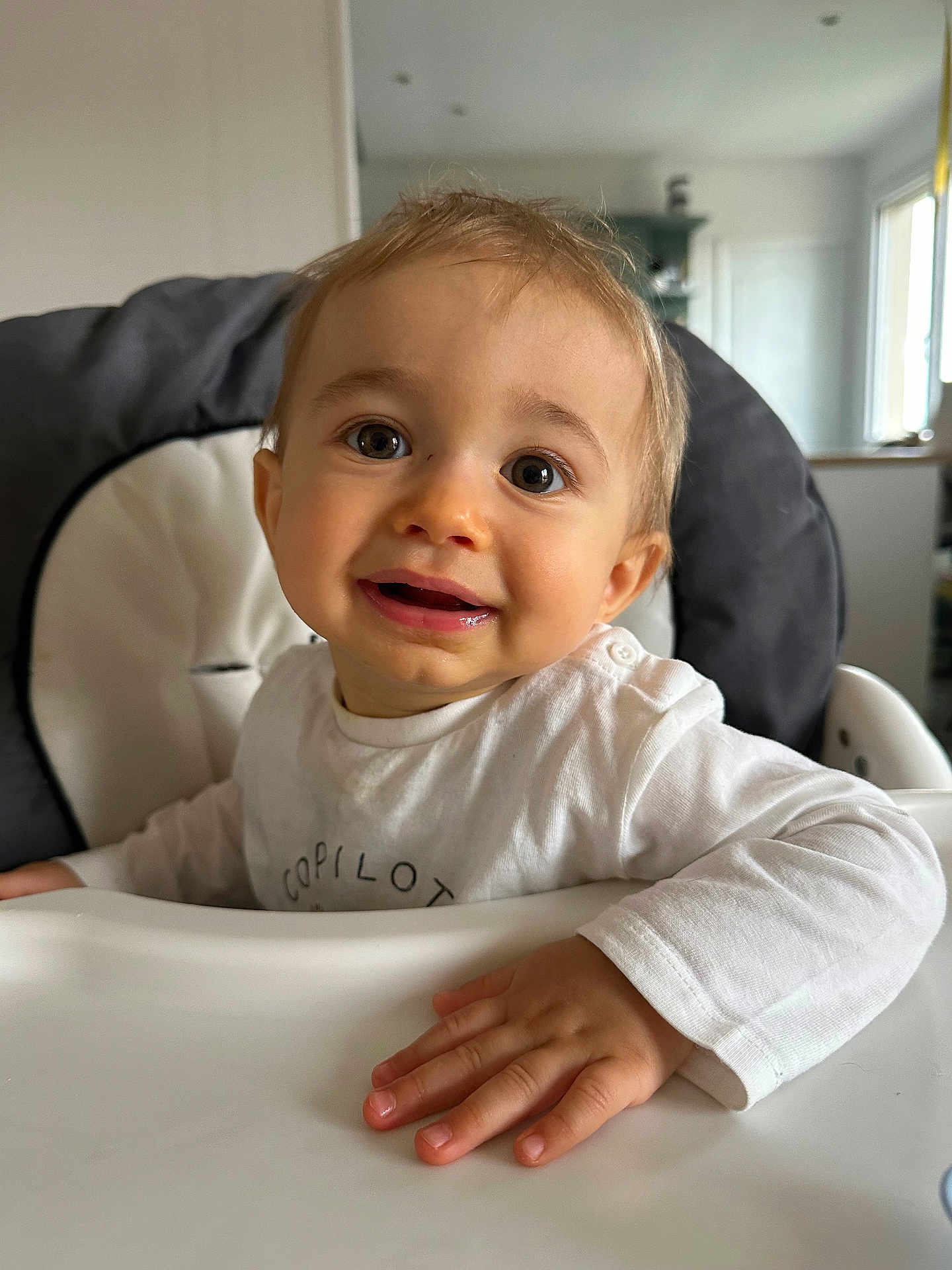 Maé a rejoint le concours — aidez-le/la à gagner de superbes lots ! toddler, child, high_chair, smile, happy, face, hand, white_shirt, indoor, baby, person, cute, expression, young_child, skin, eyes, mouth, furniture, room, home