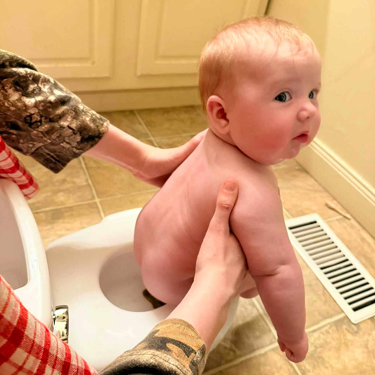 Anastasia is registered to the contest to win money with this photo: baby, child, potty, bathroom, tile_floor, cabinet, hands, person, support, curious, skin, naked, infant, floor_vent, plumbing, parent, care, indoor, young, gaze