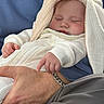 baby, sleeping, infant, white_clothing, bunny_ears, hand, adult, bracelet, blue_jacket, cozy, closeup, peaceful, cuddling, portrait, soft_light, fingers, skin, person, rest, comfort