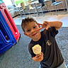 child, boy, ice_cream, peace_sign, indoor, playground_equipment, chairs, smiling, shorts, tshirt, floor, window, daylight, happy, casual_clothing, fun, play, food, portrait, cute