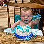 Bryson joined the competition — help win amazing prizes! baby, toddler, cake, birthday_cake, messy, high_chair, blue_frosting, white_cake, child, smiling, face, hand, wooden_background, celebration, party, food, dessert, sitting, happy, adult_hand