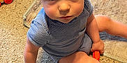 Bryson is registered to the contest to win money with this photo: child, toddler, indoor, carpet, toy, person, blue_eyes, blonde_hair, striped_clothing, sitting, floor, playtime, cute, looking_up, baby_toys, carpet_texture, casual_wear, young_child, home, curious_expression