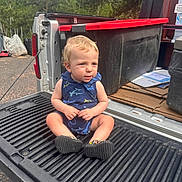 Bryson is registered to the contest to win money with this photo: toddler, child, blonde_hair, blue_outfit, shark_pattern, sitting, truck_tailgate, outdoor, trees, greenery, cardboard, plastic_container, curious, shoes, daylight, casual, parked_vehicle, nature, photography, young_child