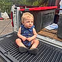 toddler, child, blonde_hair, blue_outfit, shark_pattern, sitting, truck_tailgate, outdoor, trees, greenery, cardboard, plastic_container, curious, shoes, daylight, casual, parked_vehicle, nature, photography, young_child