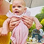 baby, child, infant, pink_dress, smiling, happy, outdoor, garden, umbrella, adult_hands, yellow_dress, table, glass, plate, feeding_bottle, high_chair, food, drink, summer, daylight