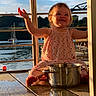 Dorothea is registered to the contest to win money with this photo: barefoot, child, hand_raised, happy, metal_pot, nature, outdoor, playful, polka_dot_dress, portrait, reflection, sailboats, sky, smiling, summer, sunlight, toddler, trees, water, wooden_dock