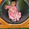 Dorothea is registered to the contest to win money with this photo: child, curious, cute, daylight, expression, face, fun, grass, nature, outdoor, person, pink_dress, play, playground, shoe, sitting, toddler, tunnel, wood, young