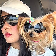 London Le King is registered to the contest to win money with this photo: woman, dog, sunglasses, cap, car_interior, pet, bow, long_hair, light, portrait, closeup, fashion, accessories, cute, small_dog, companion, seat, casual, travel, reflection
