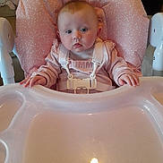 Paisley is registered to the contest to win money with this photo: baby, high_chair, pink, child, infant, face, hands, clothing, indoor, seat, tray, curious, straps, cute, young, person, portrait, expression, cozy, pastel