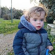 Esteban participe au concours pour gagner de l'argent avec cette photo : child, toddler, winter_jacket, blue_jacket, outdoor, park, bench, grass, trees, curly_hair, blue_eyes, nature, daylight, pathway, holding, handle, cold_weather, expression, portrait, young