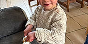 Esteban participe au concours pour gagner de l'argent avec cette photo : toddler, child, playing, tambourine, indoor, kitchen, sweater, wooden_chair, couch, floor_tiles, smiling, blonde_hair, toy, person, happy, casual_clothing, furniture, home, cute, curly_hair