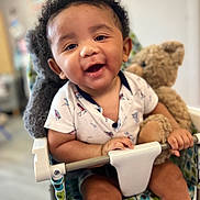 Brighton is registered to the contest to win money with this photo: baby, child, smiling, teddy_bear, seat, patterned_fabric, indoor, happy, cute, infant, person, face, hand, clothing, toy, closeup, portrait, baby_chair, holding, curly_hair
