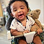 baby, child, smiling, teddy_bear, seat, patterned_fabric, indoor, happy, cute, infant, person, face, hand, clothing, toy, closeup, portrait, baby_chair, holding, curly_hair